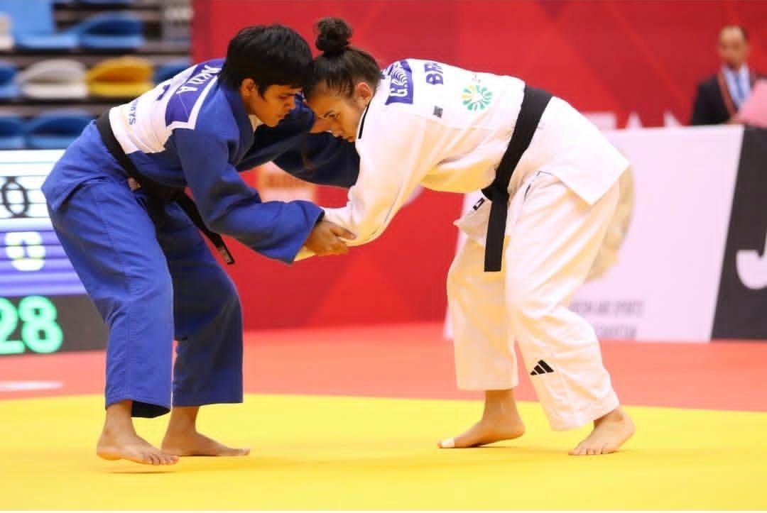 Duas judocas disputam a pegada durante combate, uma de judogi azul e outra de branco